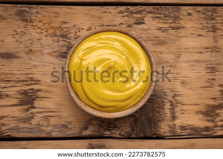 Sauce bowl with delicious mustard and seeds on wooden table, top view