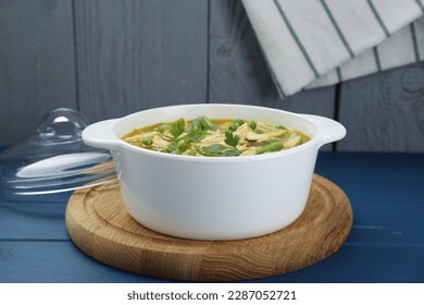 Saucepan of delicious vegetable soup with chicken on blue wooden table