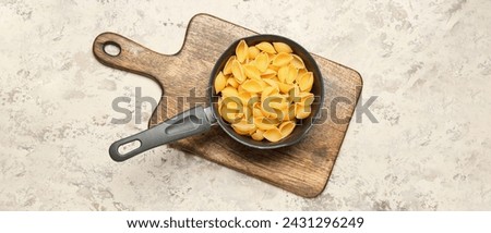 Saucepan with raw conchiglie pasta on grey grunge background