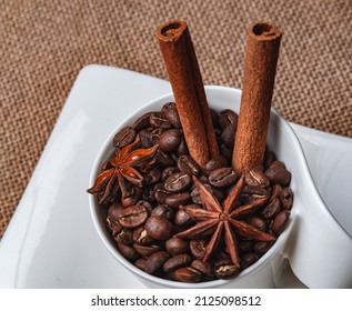 A Saucer With A White Cup On The Table. The Cup Contains Coffee Beans, Two Cinnamon Sticks And Two Star Anise.View From Above.Copy Space.