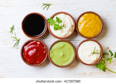 Sauces ketchup, mustard, mayonnaise, wasabi, soy sauce in clay bowls on wooden white background