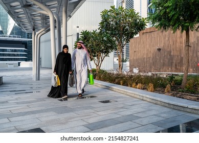 Saudi Arab Couple Shopping Outdoor Carrying Mall Bags. Muslim Family Walking Happy In Summer Enjoying The Gifts Wearing Abaya And Traditional Dress