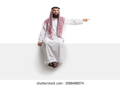 Saudi Arab Man Sitting On A Blank Panel And Pointing Isolated On White Background