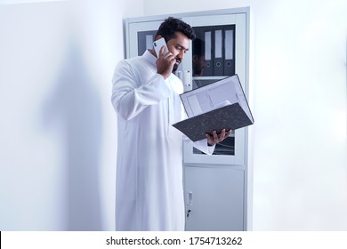 Saudi Arab Man Speaking On Phone While Looking In File In Office