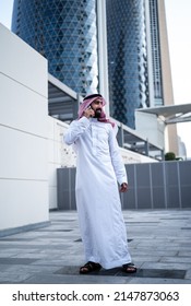 Saudi Arab Man Standing Talking On Mobile Phone Outdoor. Muslim Businessman From Saudi Arabia Wearing Traditional Dress Standing