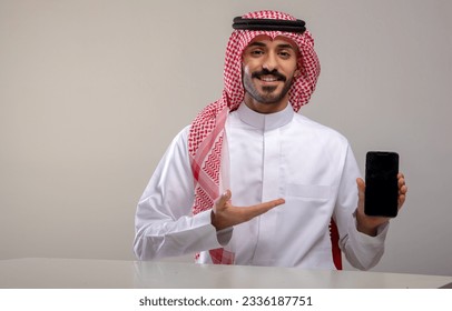 A Saudi character holding a phone sitting in the office on a white background - Powered by Shutterstock