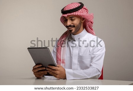 A Saudi character holding a tablet sitting in the office on a white background