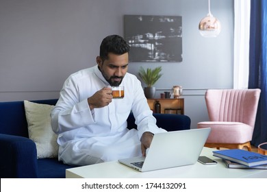 Saudi Man Drinking Tea In Living Room At Home Using Laptop 