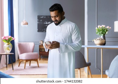 Saudi Man Standing In Living Room At Home Using Phone