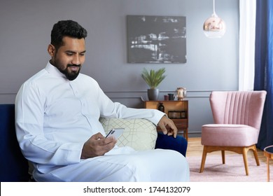 Saudi man using phone at home sitting at sofa in living room