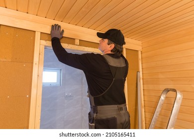 Sauna Construction, Finishing. The Man Is Screwing A Wooden Bench To The Wall.