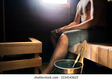 Sauna in Finland. Man relaxing in steam room in health spa, cabin, home or wellness hotel. Traditional Finnish summer. Old wood interior. Water bucket and ladle. Hot temperature therapy.