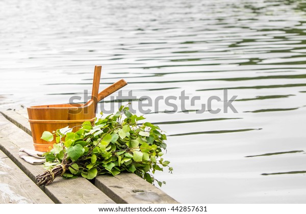 Sauna\
whisk and wooden bucket next to lake. Sauna equipment on the pier.\
Traditional Finnish summer. Empty spacefor\
text.