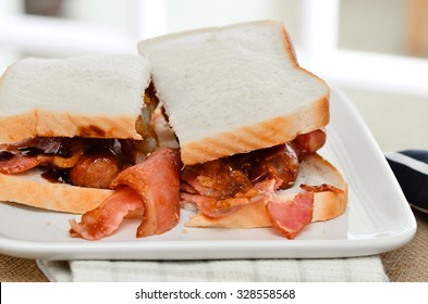 Sausage And Bacon Sarnie With Brown Sauce On White Bread.