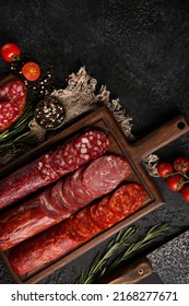 Sausage And Cold Cuts. Types Of Different Loaf Sausages On An Old Wooden Board On Black Background And Burlap With Cherry Tomatoes, Rosemary, Garlic And Spices.Rustic.Top. Background Image, Copy Space