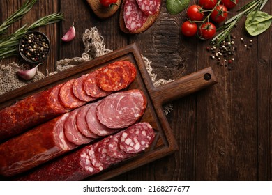 Sausage and cold cuts. Types of different loaf sausages on an old wooden background and burlap with cherry tomatoes, rosemary, garlic and spices. Rustic. Top. Background image, copy space