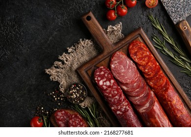 Sausage And Cold Cuts. Types Of Different Loaf Sausages On An Old Wooden Board On Black Background And Burlap With Cherry Tomatoes, Rosemary, Garlic And Spices.Rustic.Top. Background Image, Copy Space