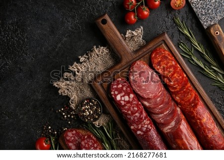 Sausage and cold cuts. Types of different loaf sausages on an old wooden board on black background and burlap with cherry tomatoes, rosemary, garlic and spices.Rustic.Top. Background image, copy space