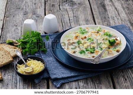 Sausage Vegetable Chowder, thick cheesy soup with chunks of broccoli, carrot, potato in white bowl on rustic wood table with slices of bread, horizontal view, not AI generated
