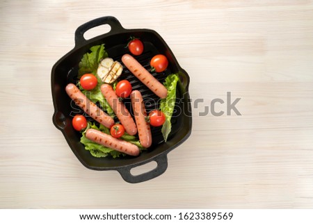 Sausages in a cast-iron pan, with tomatoes, lettuce, fried garlic. Top view, copy space.