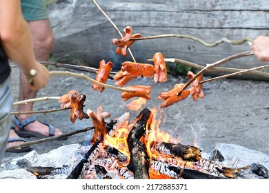 Sausages and fire. Outdoor grilling of many sausages pierced on a toasting stick over a campfire. Close-up on toasted food. The closeup of cooking sausage on fire. - Powered by Shutterstock