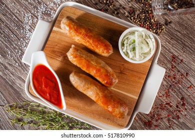 Sausages grilled on a wooden board with a white plate, spices and vokruk razmarin, fasfud concept