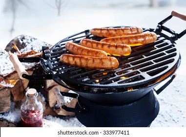 Sausages grilling over a hot fire in a portable BBQ outdoors in snow in winter, conceptual of a winter grill party