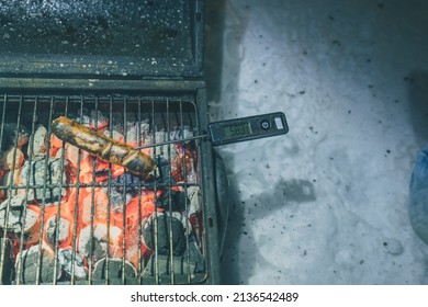 Sausages On A Grill, Visible One Burnt Sausage On A Charcoal Grill With Temperature Meter Sticked Inside. Reading Of 58 Degrees.