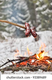 Sausages on the stick grilled in the fire. Winter forest.