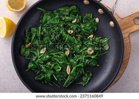Sauteed garlic spinach in a cooking pan with slices of crispy garlic, healthy side dish idea