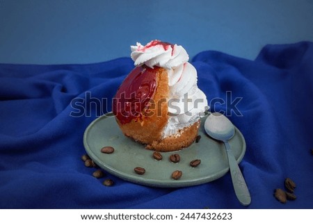 Savarin cake with red glaze and whipped cream on blue cloth background 