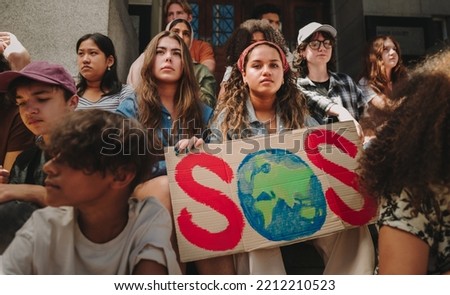 Save our planet campaign. Group of multicultural climate activists sitting with posters outside a building. Youth demonstrators protesting against global warming and climate change.