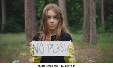 Save The Planet For Future. Portrait Of A Sweet Teen Girl Showing A Sign Protesting Against Plastic Pollution In The Forest. No Plastic Concept. Eco-friendly Environment.