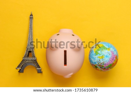 Save up for a trip. Piggy bank with a figure of the Eiffel tower, globe on yellow background. Top view