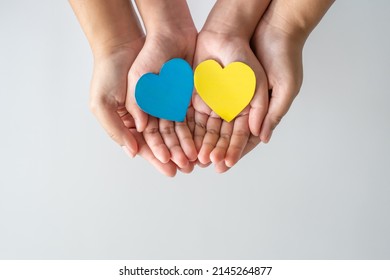 Save Ukraine Stop The War. Adult And Child Hands Holding Paper Heart In The Color Of National Flag Of Ukraine. Concept Of Togetherness.