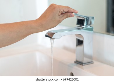 Save the water concept.Hand closing valve on sink in bathroom. Water dripping to stop running as hand turn off the faucet.Detect-a-Leak week.