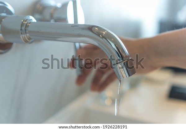 Save the water concept.Hand closing valve on sink\
in bathroom. Water dripping to stop running as hand turn off the\
faucet. Detect a Leak\
week.