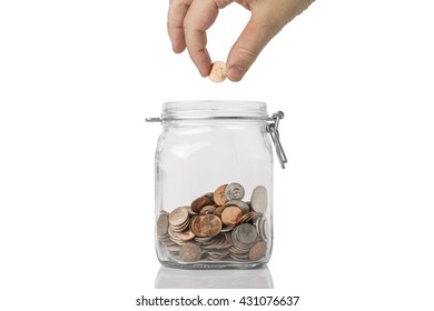 Saving Concept - A Jar Of American Coins With A Hand About To Drop A Penny Into It.