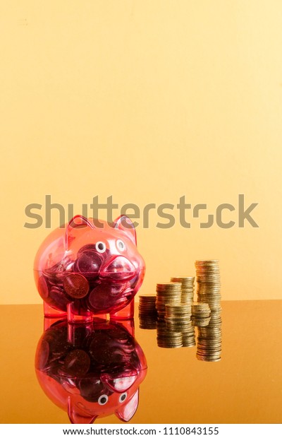 Saving Concept with red piggy bank and coins\
stacked on a yellow\
background.