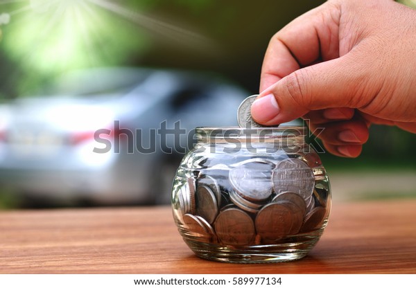 saving money for
buy car concept, male hand putting money coin in to piggy back over
car background with
sunlight