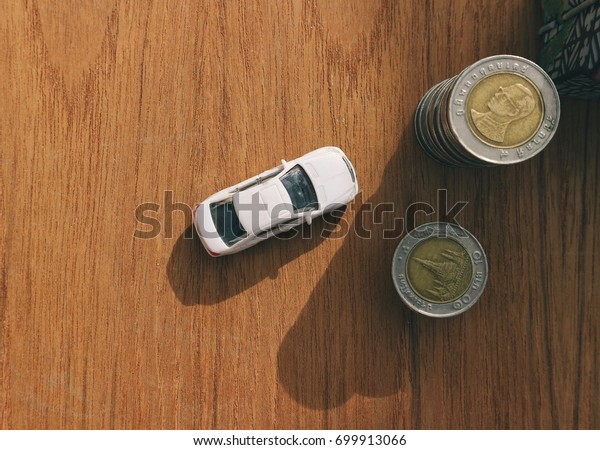 Saving money for car\
concept, white toy car and rolls of money in shadow sunlight,\
pattern wood table