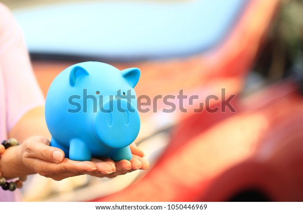 Saving\
money for car concept, Young woman holding blue piggy with standing\
at the car parking lot background, Auto\
business