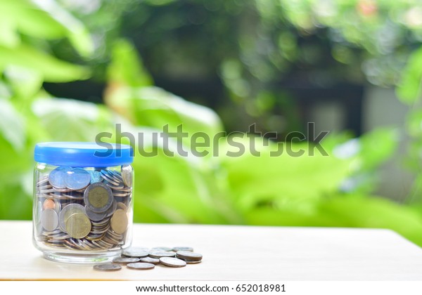 Saving money with\
coin for growing your business,Thai\'s coin in a glass jar on wooden\
texture,saving for good future life,coin  before green\
background.Saving for a new\
car.