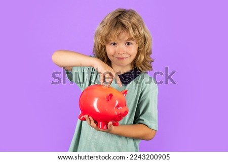 Saving money concept. Portrait of a little boy putting money on a moneybox. Child saving money in a piggybank on studio background.