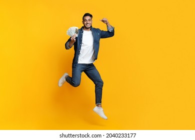 Saving Money, Gambling, Gaming, Trading, Loan Concept. Positive Middle-eastern Guy Holding Bunch Of Money And Raising Fist Up, Won Lottery, Yellow Studio Background, Full Length, Copy Space