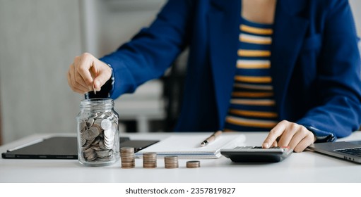 saving money with hand putting coins in jug glass and calculator to calculate budget concept finance and accounting and Gantt chart diagram. in office - Shutterstock ID 2357819827