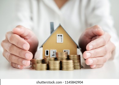 Saving money for house and real estate. Woman hand protecting on  stack coins and house model on table.