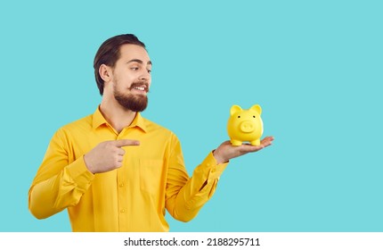 Saving Money And Making Profit. Man With Piggy Bank Offers To Make Favorable Financial Bank Offer Or Make Profitable Purchase. Joyful Man Pointing Finger At Piggy Bank In Hand On Light Blue