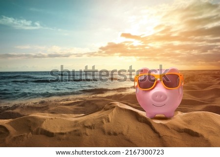 Saving money for summer vacation. Piggy bank with sunglasses on sandy beach near sea at sunset, space for text