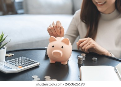 Saving money wealth concept, asian young business woman hand putting coin into piggy for saving cost, cash finance planning to spend enough money on her income for save money, payment tax, investing. - Powered by Shutterstock